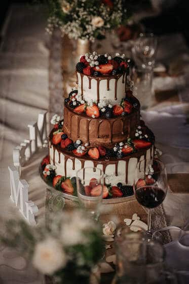 Svadobná nahá torta so striedajúcimi sa korpusmi a stekajúcou mliečnou čokoládou, poschodia zdobí lesné ovocie.